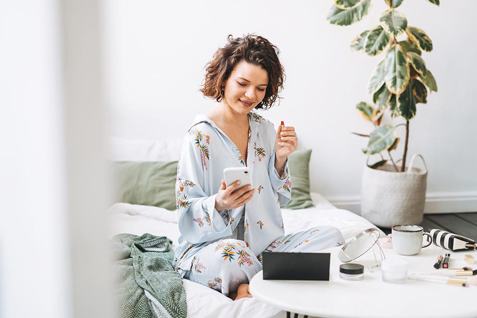 Dame op bed zittend met make-up materialen kijkend op haar telefoon